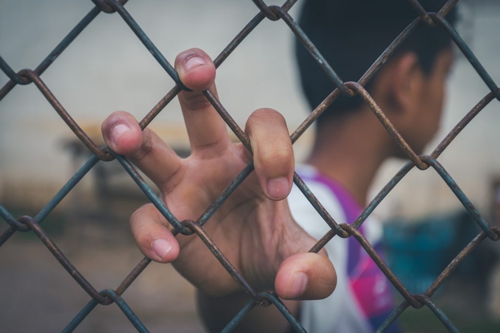 Asian young boy holding hand on a metal chain wire mesh fence