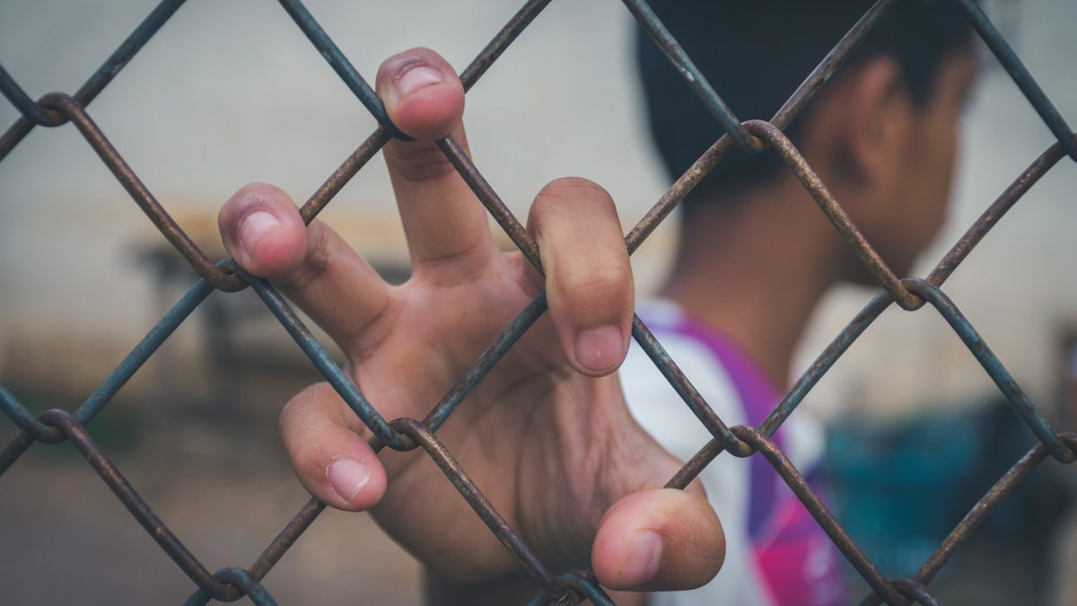 Asian young boy holding hand on a metal chain wire mesh fence